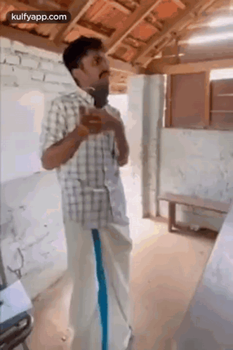 A Man In A Plaid Shirt And Blue Pants Is Standing In A Room With A Microphone In His Hand . GIF