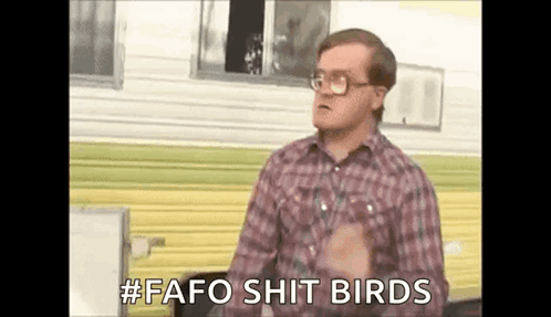 A Man In A Plaid Shirt And Glasses Is Standing In Front Of A Trailer And Talking . GIF
