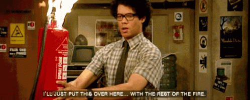 A Man In A Plaid Shirt And Tie Holds A Red Spray Foam Fire Extinguisher In Front Of Him GIF