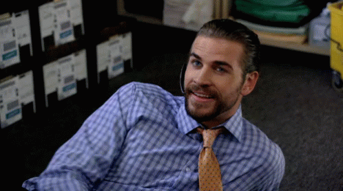 A Man In A Plaid Shirt And Tie Is Laying On The Floor Smiling GIF