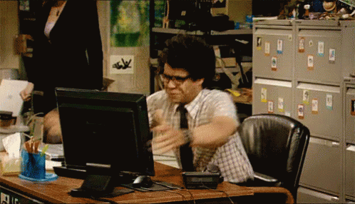 A Man In A Plaid Shirt And Tie Is Sitting At A Desk In Front Of A Computer GIF