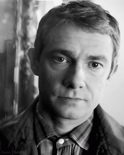 A Man In A Plaid Shirt And Tie Looks At The Camera In A Black And White Photo . GIF