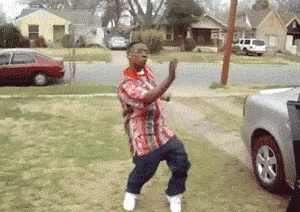 A Man In A Plaid Shirt Is Dancing In Front Of A Silver Truck . GIF
