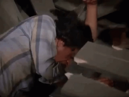 A Man In A Plaid Shirt Is Drinking From A Faucet In A Bathroom . GIF