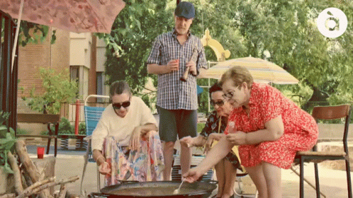 A Man In A Plaid Shirt Is Holding A Bottle Of Beer While A Group Of People Sit Around A Pan GIF
