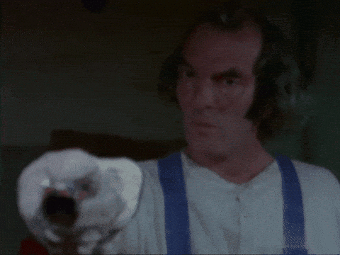 A Man In A Plaid Shirt Is Holding A Gun In His Hand . GIF