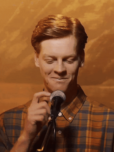 a man in a plaid shirt is holding a microphone and smiling