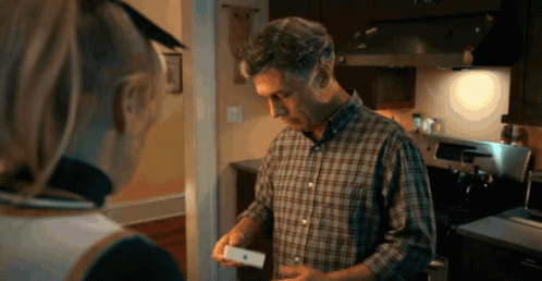 A Man In A Plaid Shirt Is Holding An Apple Product In His Hand GIF