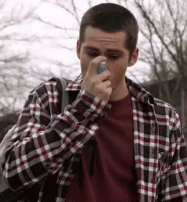 A Man In A Plaid Shirt Is Holding An Asthma Inhaler To His Nose . GIF