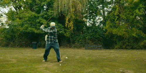 A Man In A Plaid Shirt Is Jumping In The Air In A Park GIF