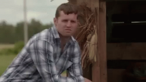 A Man In A Plaid Shirt Is Leaning Against A Wooden Fence . GIF