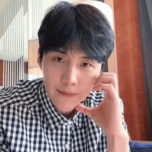 A Man In A Plaid Shirt Is Looking At The Camera With His Hand On His Face GIF