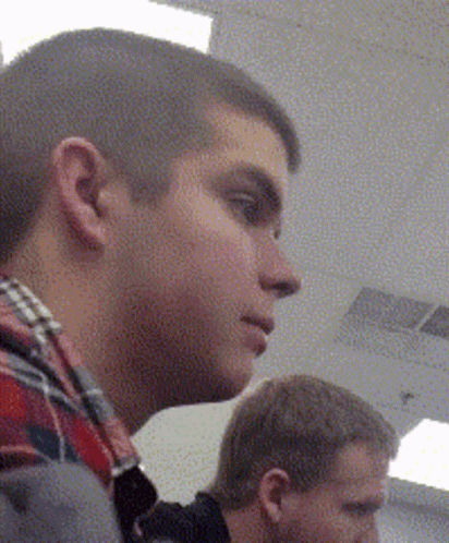 A Man In A Plaid Shirt Is Looking To His Left GIF