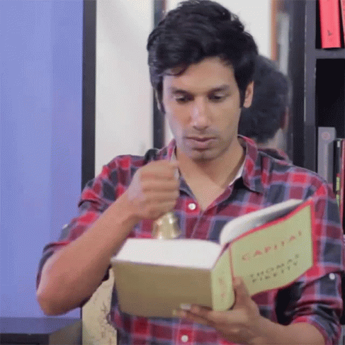 A Man In A Plaid Shirt Is Reading The Book Capital GIF