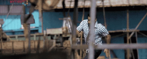 A Man In A Plaid Shirt Is Running Through A Fence With The Word Mythri On The Bottom Right GIF