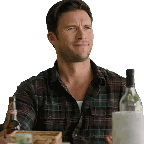 a man in a plaid shirt is sitting at a table holding a bottle