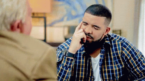 A Man In A Plaid Shirt Is Sitting At A Table With A Man In A Tan Jacket . GIF