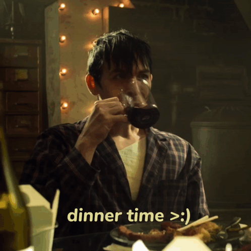 A Man In A Plaid Shirt Is Sitting At A Table With A Plate Of Food And Says Dinner Time > :) GIF