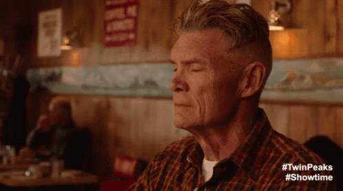 A Man In A Plaid Shirt Is Sitting At A Table With His Eyes Closed In A Diner . GIF