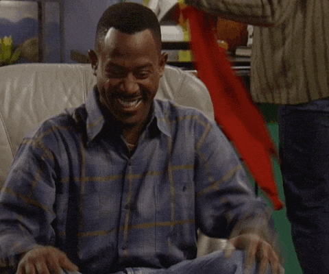 A Man In A Plaid Shirt Is Sitting In A Chair And Laughing GIF