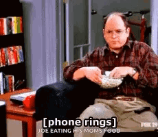 A Man In A Plaid Shirt Is Sitting In A Chair Eating Popcorn . GIF