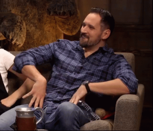 A Man In A Plaid Shirt Is Sitting In A Chair With His Hands On His Knees . GIF