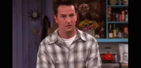 A Man In A Plaid Shirt Is Sitting In A Kitchen Looking At The Camera . GIF