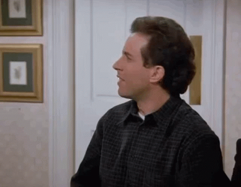 A Man In A Plaid Shirt Is Sitting In A Room With A Door . GIF