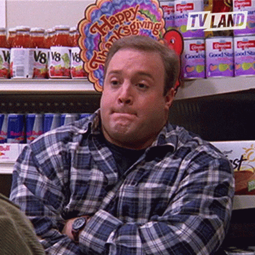 A Man In A Plaid Shirt Is Sitting In Front Of A Sign That Says Happy Thanksgiving On It . GIF