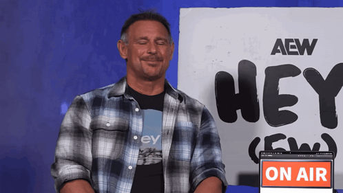 a man in a plaid shirt is sitting in front of a sign that says hey