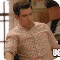 A Man In A Plaid Shirt Is Sitting In Front Of A Window And A Sign That Says Uc . GIF
