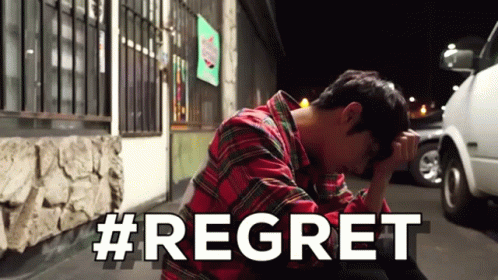 A Man In A Plaid Shirt Is Sitting On The Ground With His Head In His Hands And The Word Regret Written In White Letters GIF