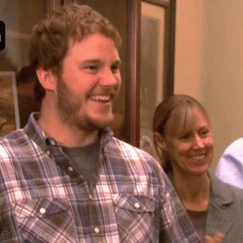 A Man In A Plaid Shirt Is Smiling While A Woman Looks On GIF