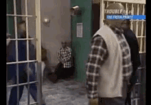 A Man In A Plaid Shirt Is Standing In A Jail Cell With Other Men . GIF
