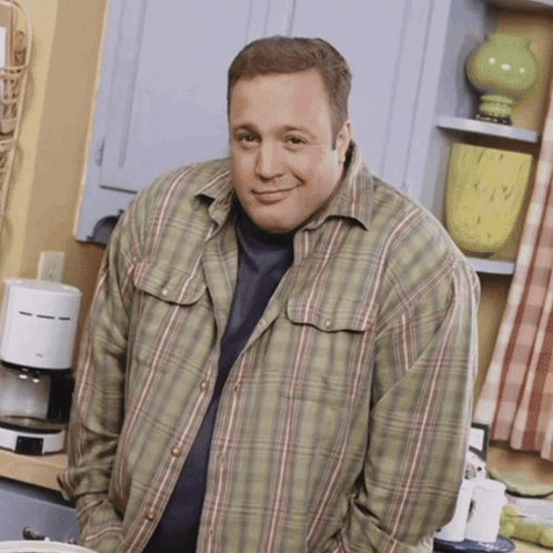 A Man In A Plaid Shirt Is Standing In A Kitchen With His Hands In His Pockets GIF