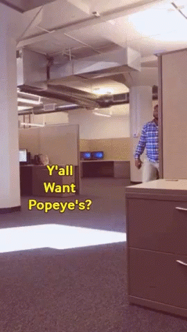 A Man In A Plaid Shirt Is Standing In An Office With The Words " Y'all Want Popeye 'S " GIF