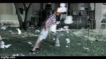 A Man In A Plaid Shirt Is Standing In Front Of A Bird Feeder Surrounded By Birds . GIF