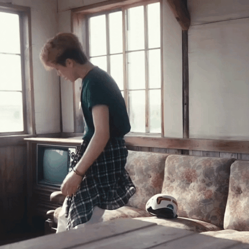 A Man In A Plaid Shirt Is Standing In Front Of A Couch GIF