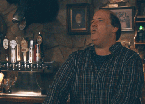 A Man In A Plaid Shirt Is Standing In Front Of A Sign That Says Well Well Well GIF