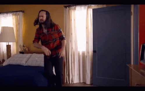 Man In Plaid Shirt Standing Next To Bed GIF