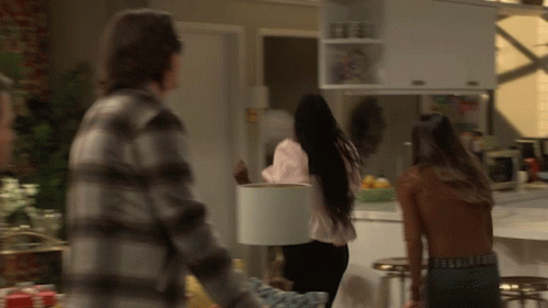 A Man In A Plaid Shirt Is Standing Next To A Woman Holding A White Lamp Shade GIF
