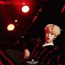 A Man In A Plaid Shirt Is Standing On A Stage With A Red Background . GIF
