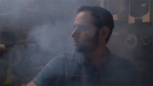 A Man In A Plaid Shirt Is Surrounded By Smoke And A Sign That Says ' A ' On It GIF