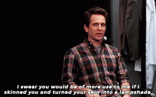 A Man In A Plaid Shirt Is Talking On A Phone While Sitting In A Chair . GIF
