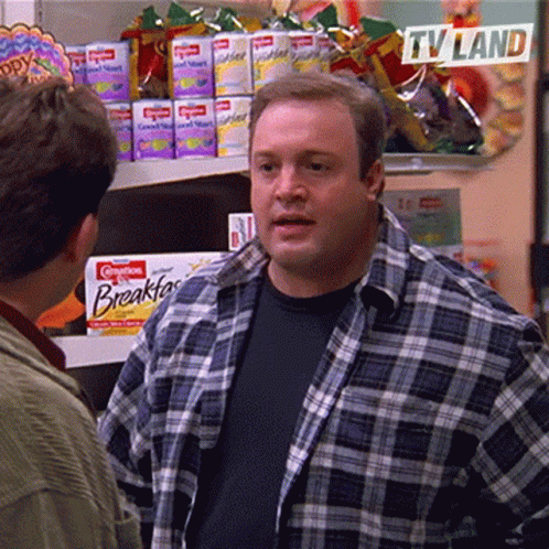 A Man In A Plaid Shirt Is Talking To Another Man In A Grocery Store With A Sign That Says Tv Land GIF