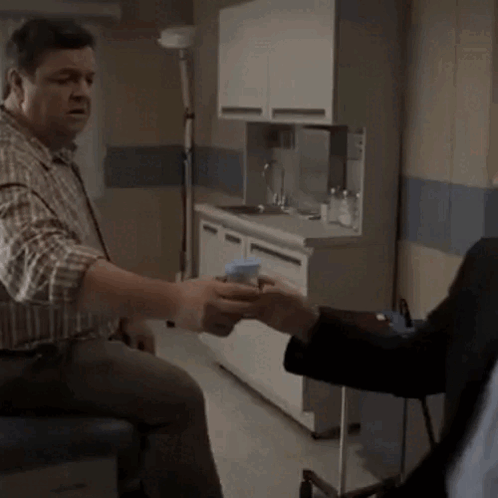 A Man In A Plaid Shirt Is Talking To Another Man In A Kitchen GIF