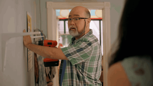 A Man In A Plaid Shirt Is Working On A Wall GIF