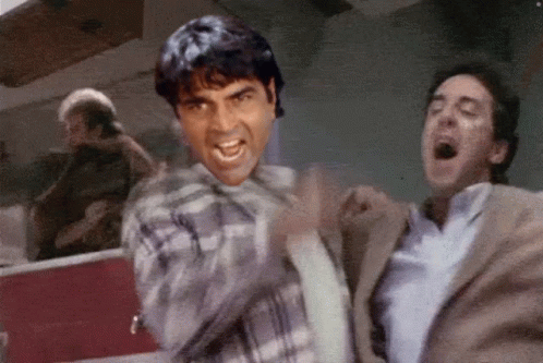 A Man In A Plaid Shirt Is Yelling At Another Man GIF