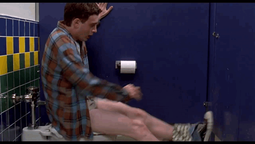 A Man In A Plaid Shirt Sits On A Toilet With His Pants Down GIF