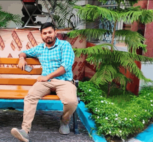 A Man In A Plaid Shirt Sits On A Wooden Bench GIF
